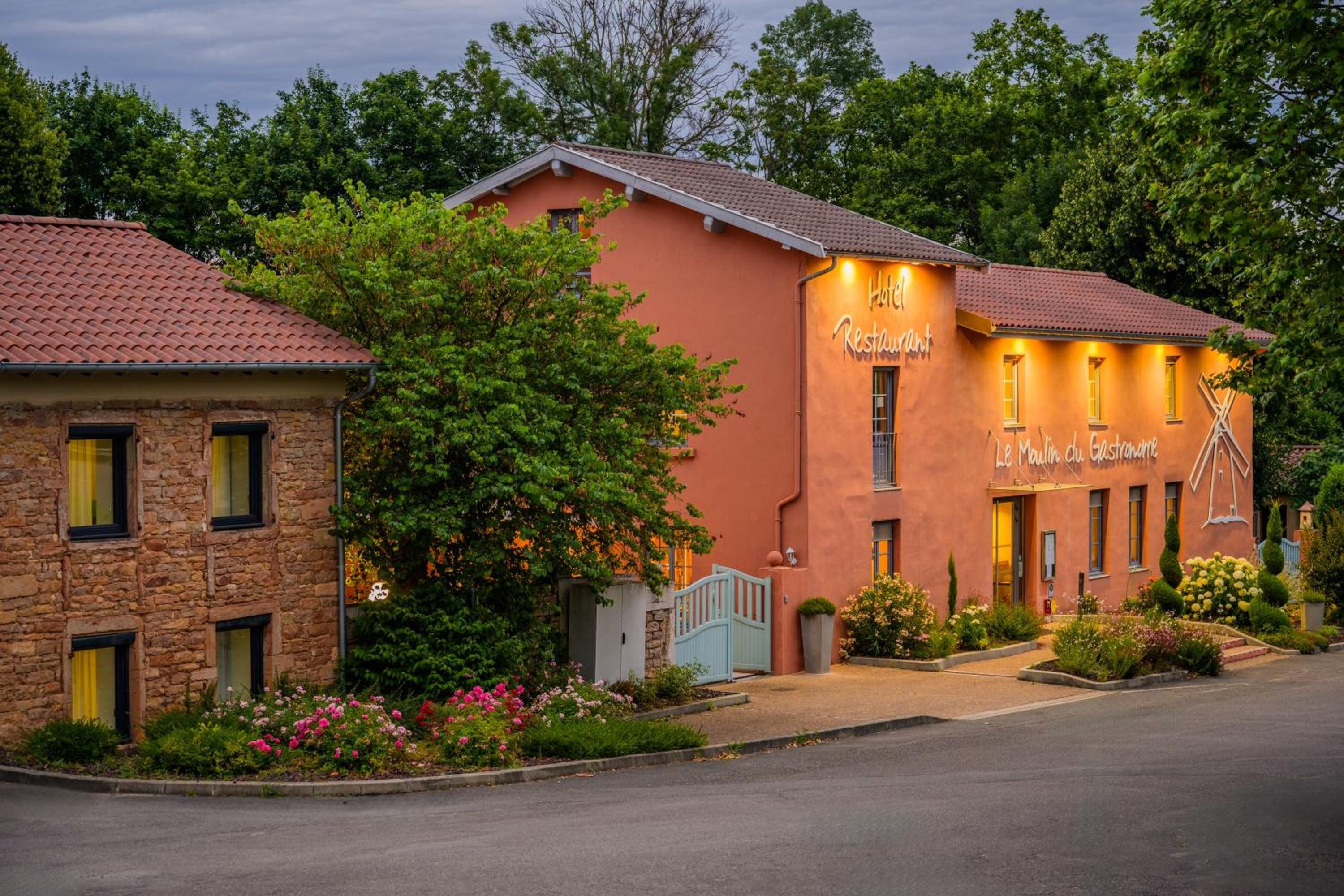 Un hôtel à la façade rouge, un bâtiment en pierre sur la gauche et une entrée bien éclairée.