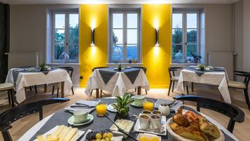 A breakfast setting with tables, chairs, and a variety of food items including fruits, cheeses, and pastries.
