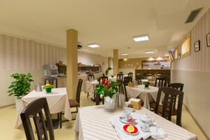 Un comedor con mesas dispuestas para el servicio, una cafetera y una cocina al fondo.