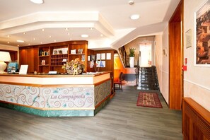 Un espace d’accueil comprenant un comptoir de réception en bois, un présentoir avec un bord décoratif et un escalier menant à l’étage supérieur.