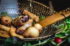 Una cesta con diversas frituras, incluyendo un alimento enrollado y varias piezas redondas, sobre una superficie con follaje al fondo.