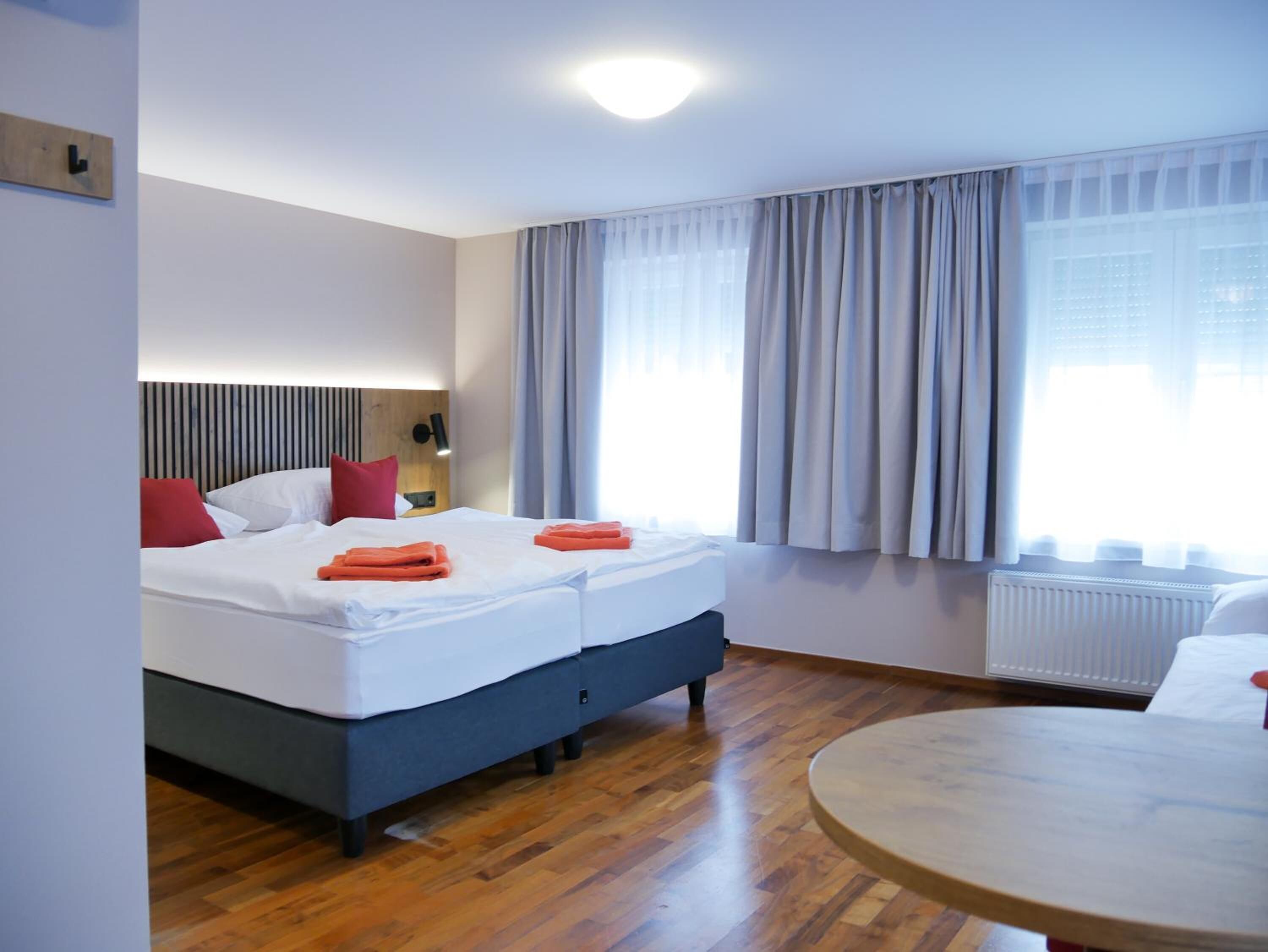 Habitación de hotel con cama, mesita de noche, lámpara y vistas al exterior a través de amplios ventanales.