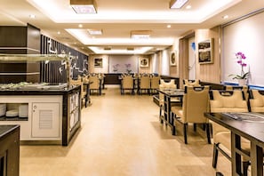 Un comedor de hotel con varias mesas y sillas, un mostrador de buffet y decoración en la pared.