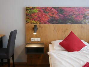 Una habitación de hotel con una cama, un escritorio, una silla, una mesita de noche y una lámpara de pared.