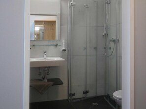 A bathroom with a glass-enclosed shower, a white sink, and a toilet. - Hotel Linde-sinohaus (Lustenau)