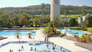 A thermal spa area with multiple pools, a central tower labeled 'THERMAL BAD ZURZACH,' and surrounding greenery.