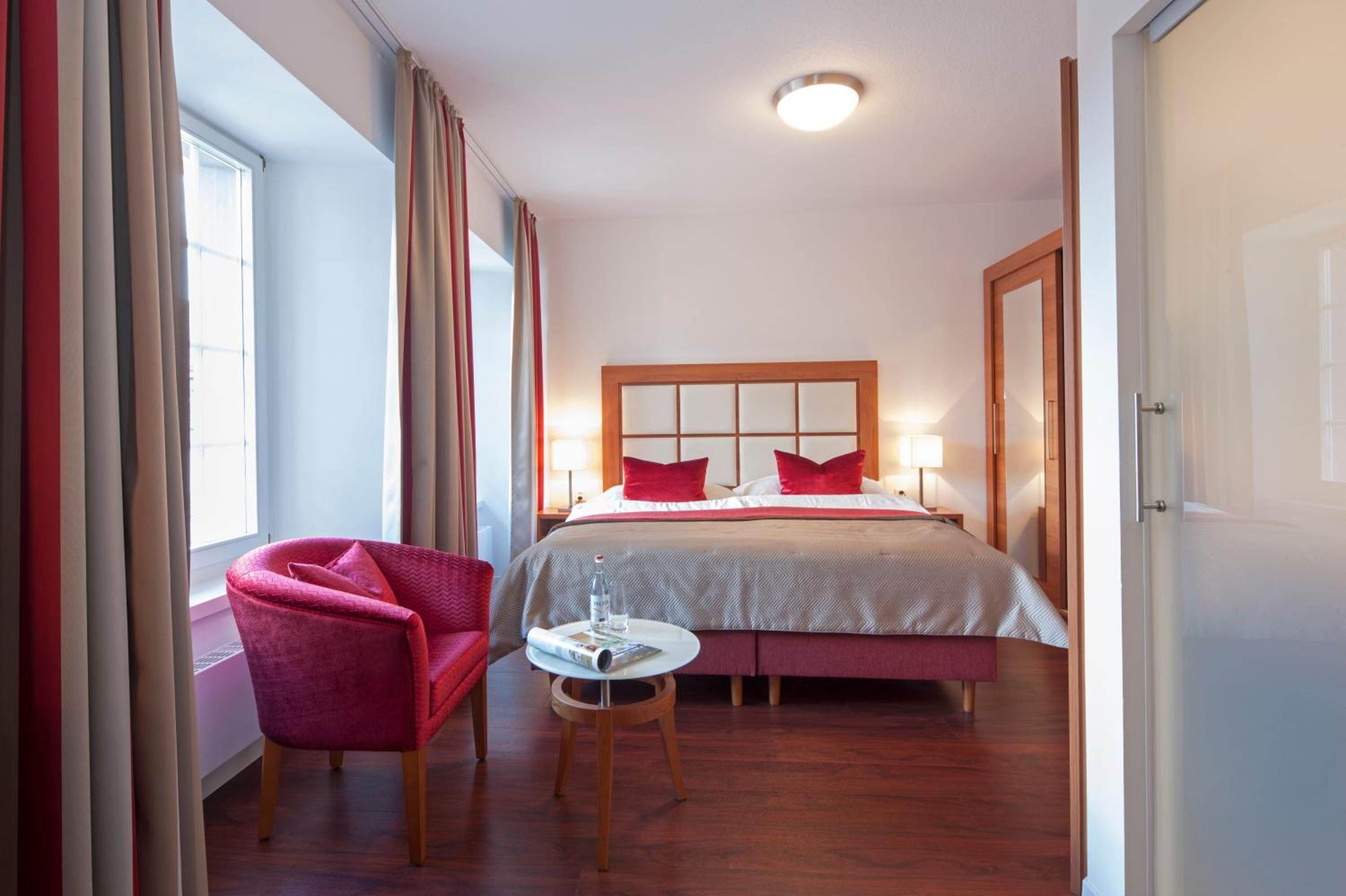 Una habitación de hotel con una cama, una silla, una mesita y una ventana con cortinas.
