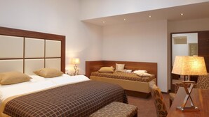 A hotel room with a large bed, a smaller bed, a desk with a lamp, and a chair.