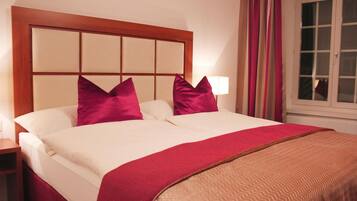 A hotel room with a large bed, a wooden headboard, two pillows, a bedside lamp, and a window with curtains.