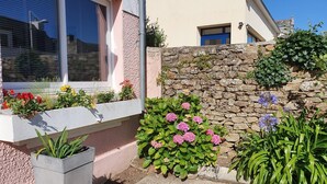 Una casa con un muro de piedra, una ventana con persianas y varias plantas en macetas.