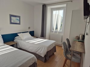 A hotel room with two beds, a desk with a chair, a radiator, and a window with curtains. - Hôtel Glann Ar Mor (Arzon)