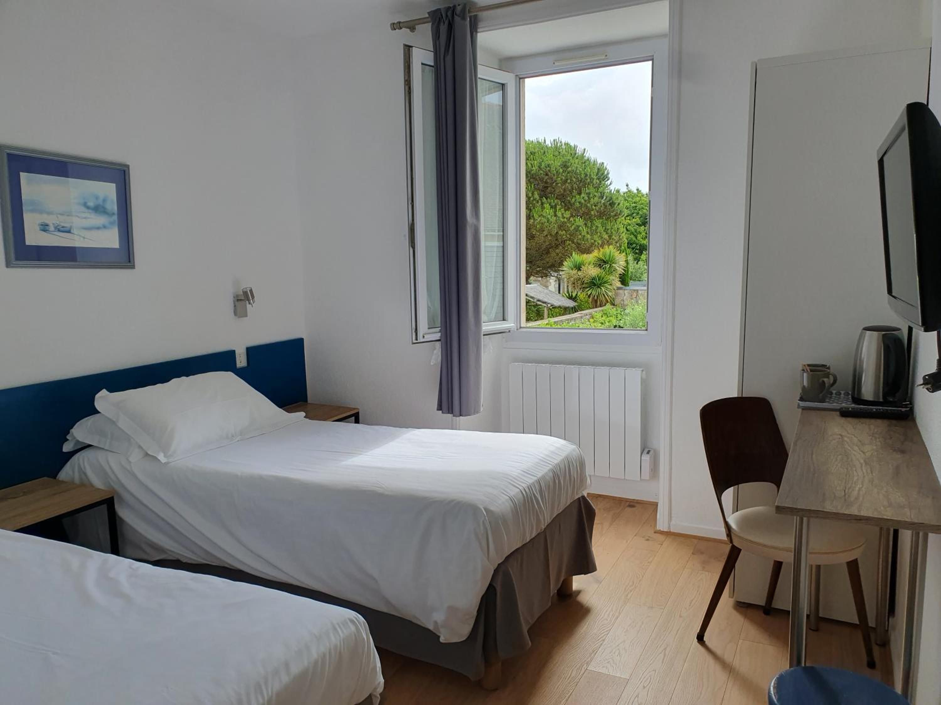 Une chambre d’hôtel avec deux lits, un bureau avec une chaise, une télévision et une fenêtre avec des rideaux.