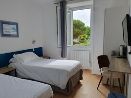 A hotel room with two beds, a desk with a chair, a television, and a window with curtains.