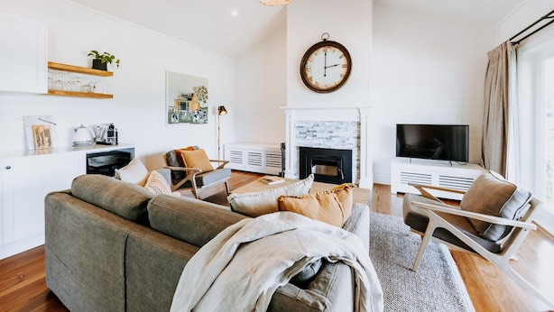 A modern living room with a sofa, armchairs, a fireplace, a television, and a clock on the wall. - The Homestead (Berry)