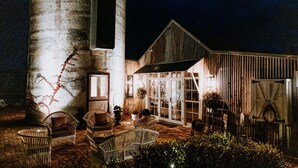 A barn-style building with large windows and a covered patio area with wicker furniture. - The Homestead (Berry)