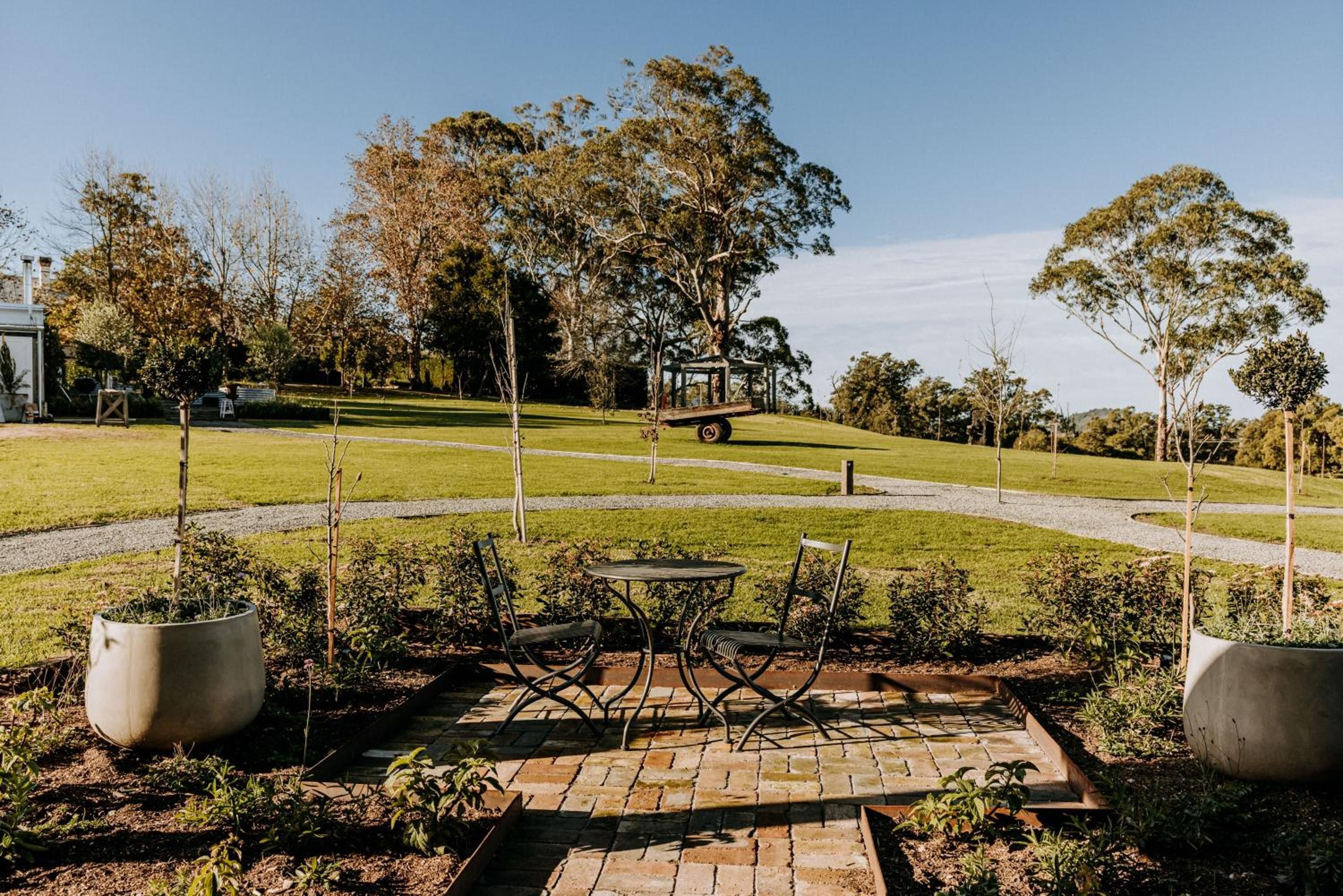 A garden patio with a table and chairs, surrounded by potted plants and a gazebo in the background.