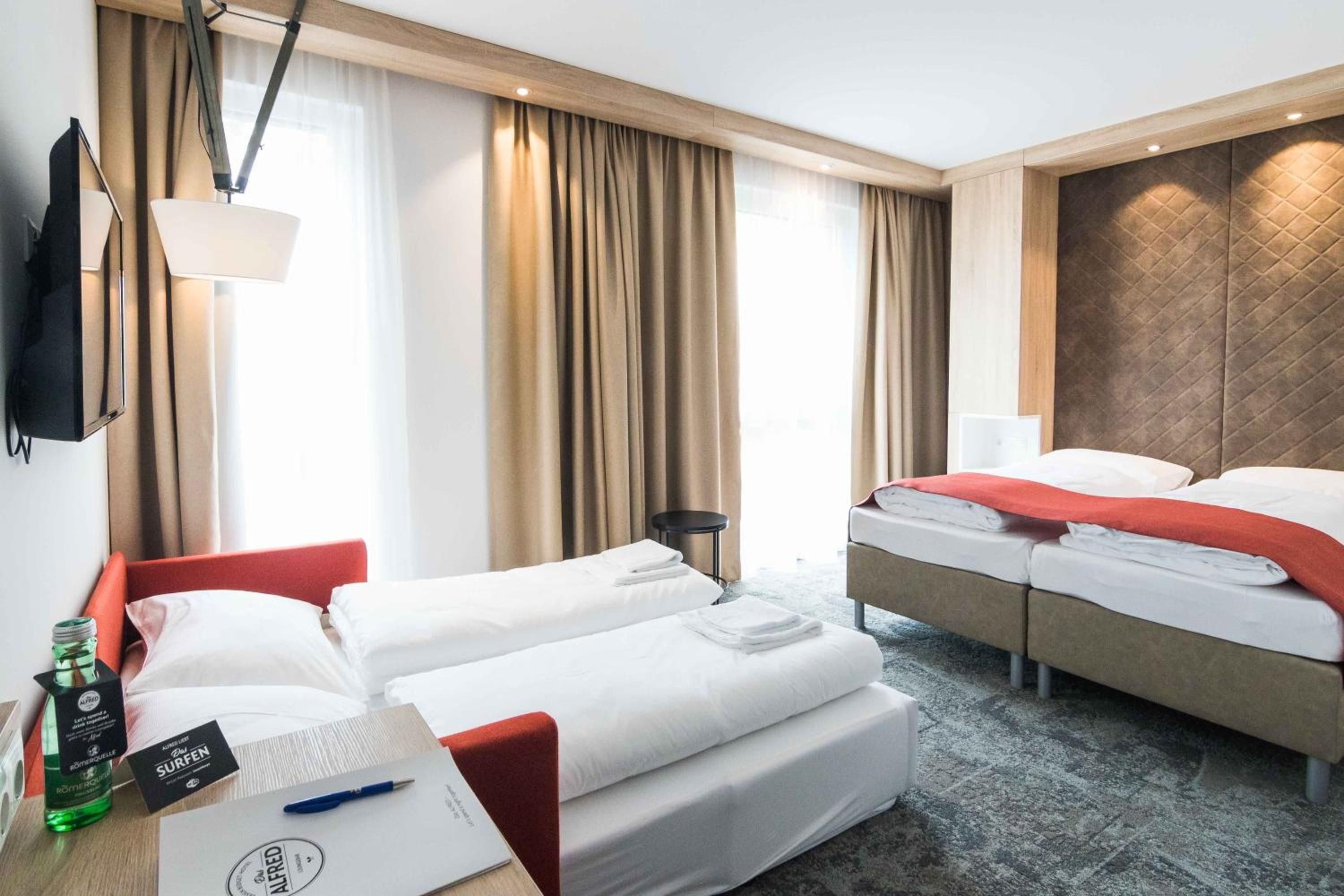 A hotel room with two beds, a desk with a laptop, a bottle, and a pen.
