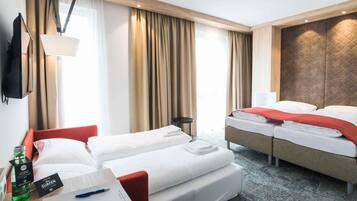 A hotel room with two beds, a desk with a laptop, a bottle, and a pen.
