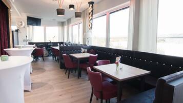 Ein Restaurant mit Tischen und Sitzbänken, einer Bühne mit Musikinstrumenten und großen Fenstern.