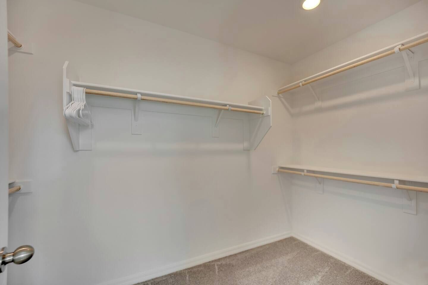 Una habitación con paredes blancas, piso alfombrado y dos estantes de madera sujetos a la pared.