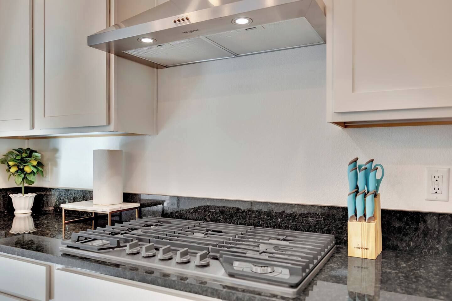 Une cuisine moderne dotée d’une cuisinière à gaz, de meubles blancs et d’un plan de travail en marbre.