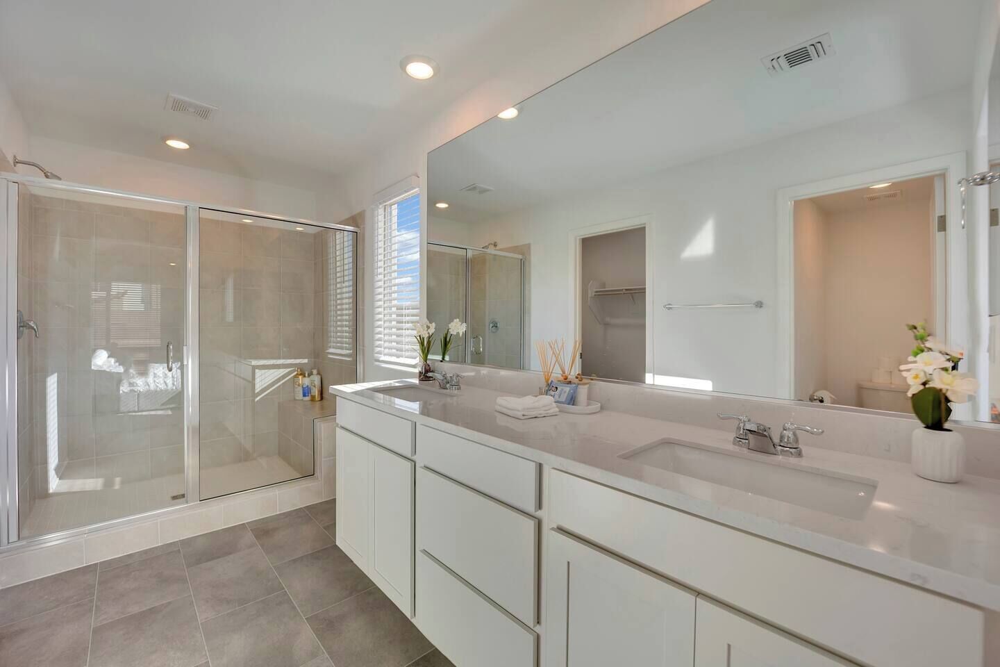 A modern bathroom with a glass-enclosed shower, a large mirror, and a dual sink vanity.