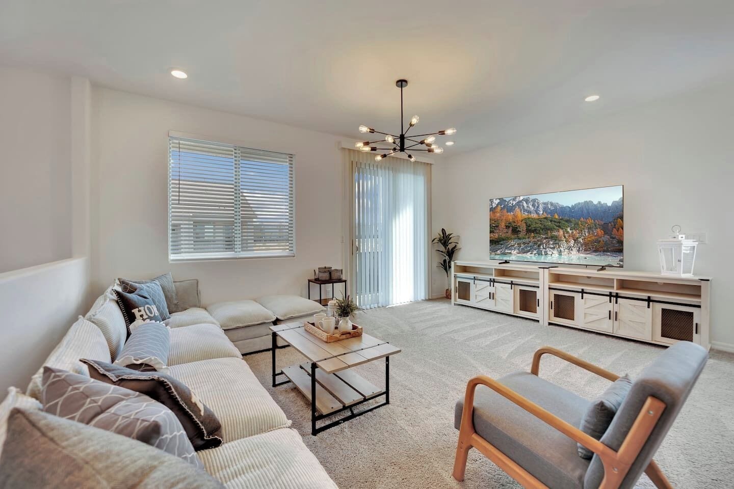 A modern living room with a sectional sofa, a coffee table, a TV, and a large window with blinds.