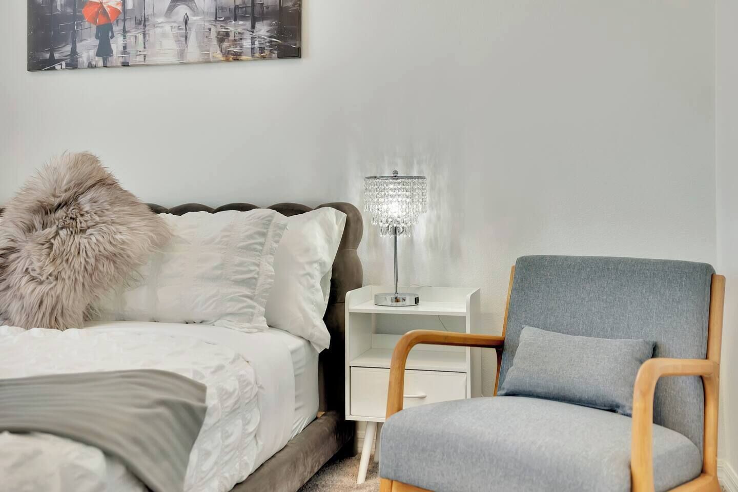 Un dormitorio con cama, una silla, una mesita de noche y una lámpara.