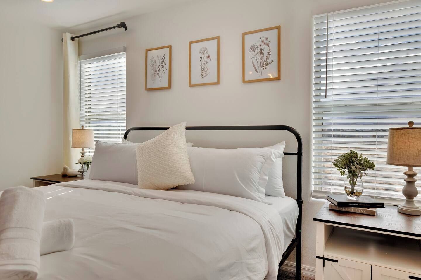 A bedroom with a bed, bedside tables, a lamp, and framed botanical prints on the wall.