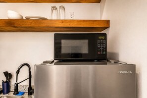 Ein Edelstahl-Kühlschrank mit einer Mikrowelle obenauf, ein blaues Reinigungstuch und ein Küchenutensilienhalter.