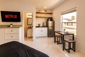 A modern hotel room with a bed, a TV mounted on the wall, a kitchenette with a refrigerator, and a dining area with a table and chairs. - #12 | Modern Island Studio | Pool | Wi-Fi | Beach (South Padre Island)