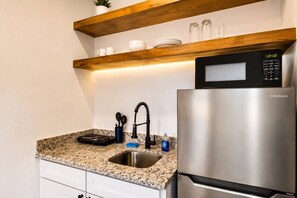 Eine Küche mit einem Edelstahlkühlschrank, einer Mikrowelle, einer Arbeitsplatte aus Granit, einem Spülbecken und Holzböden darüber.
