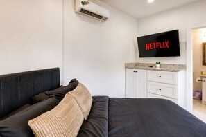 Une chambre à coucher avec un lit, un téléviseur fixé au mur et une petite commode avec des tiroirs.