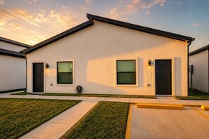 Une maison moderne de plain-pied, dotée d’un toit plat, de deux portes d’entrée et d’un petit jardin à l’avant, agrémenté d’un chemin.