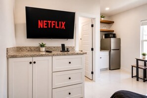 A modern kitchen with a built-in TV displaying the Netflix logo, a stainless steel refrigerator, and a countertop with a potted plant. - #12 | Modern Island Studio | Pool | Wi-Fi | Beach (South Padre Island)