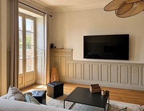 Ein Wohnzimmer mit einer Couch, einem Hocker, einem Couchtisch und einem an der Wand befestigten Flachbildfernseher.