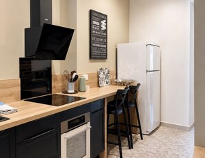 Eine moderne Küche mit Einbauofen, Kühlschrank und einer Essecke mit zwei Stühlen.