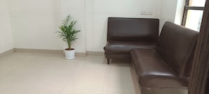 A room with a brown leather sofa, a potted plant, and a tiled floor.