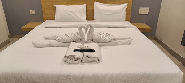 A neatly made bed with towels arranged in a swan shape and a remote control placed on the bed.