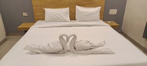 A neatly made bed with a towel arrangement in the shape of two swans, a wooden headboard, and bedside tables with lamps.