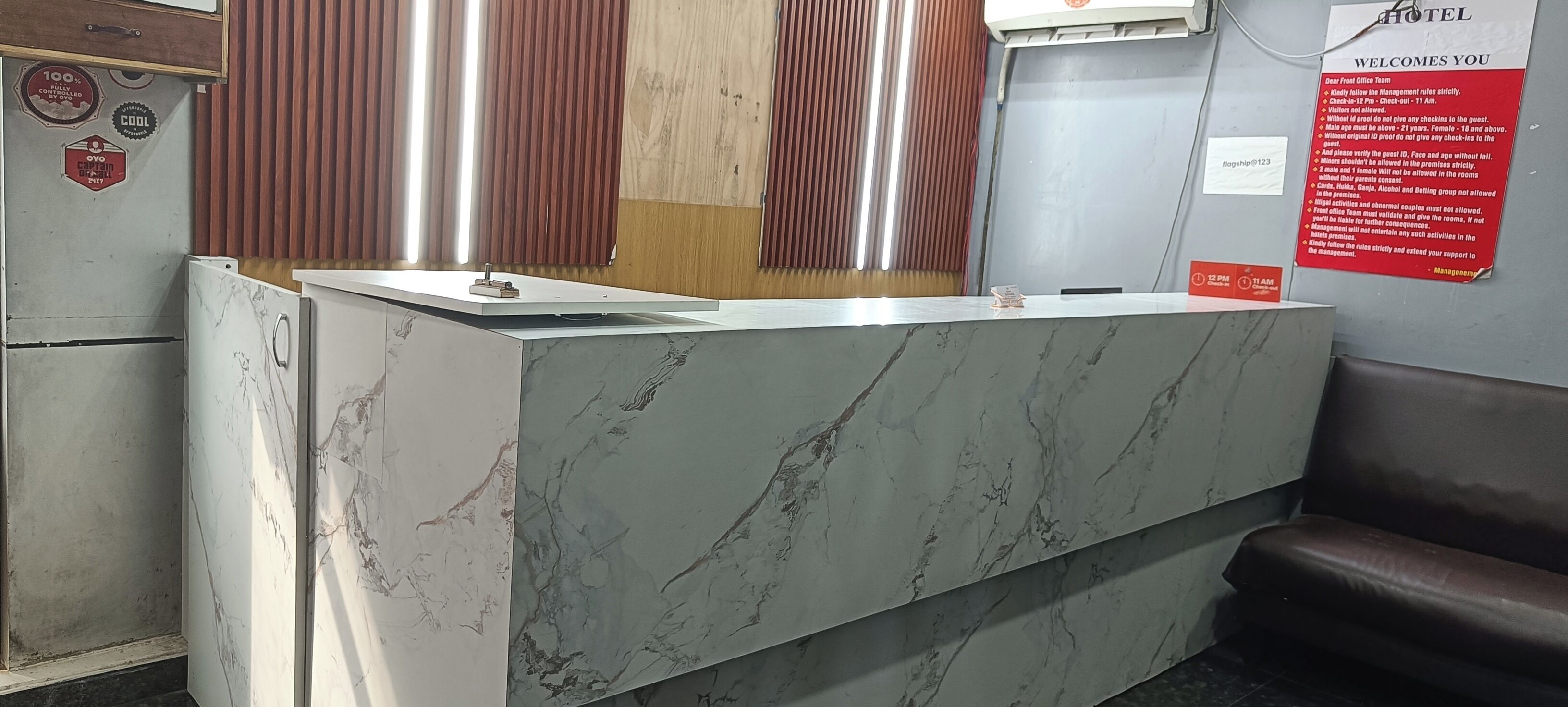 A hotel reception desk with a marble top, a wooden panel wall, and a red informational sign.