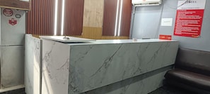 A hotel reception desk with a marble top, a wooden panel wall, and a red informational sign.