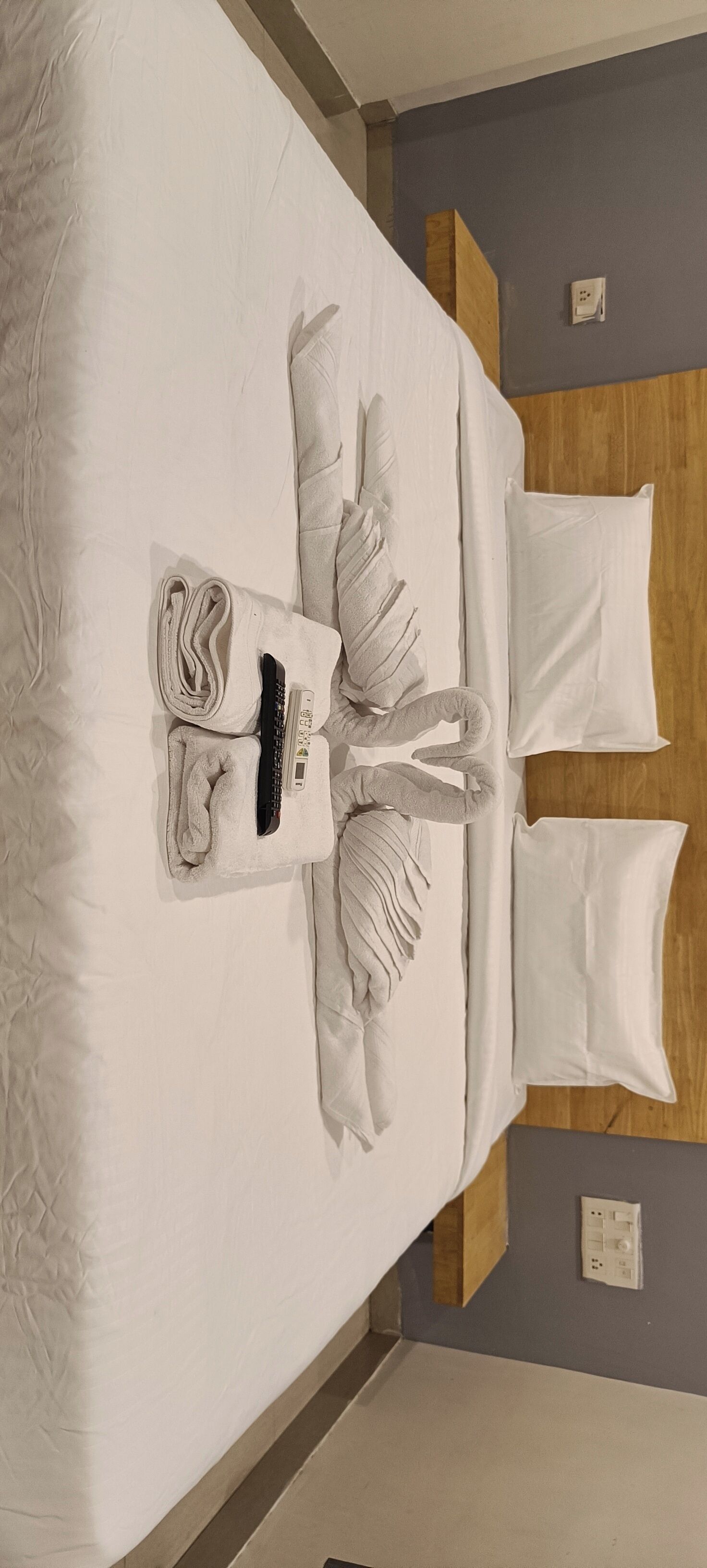 A neatly made bed with a folded towel, a remote control, and a bottle of lotion.