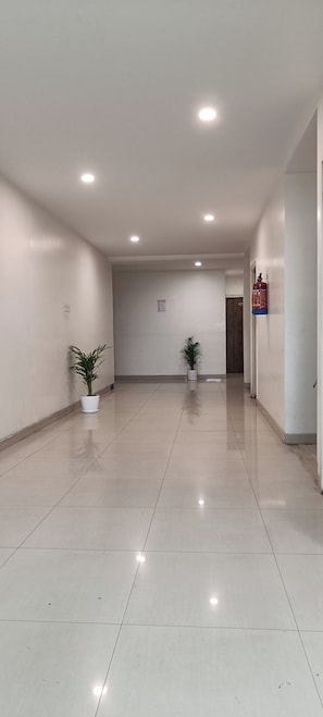 A spacious, well-lit hallway with two potted plants, a fire extinguisher, and a notice sign on the wall.
