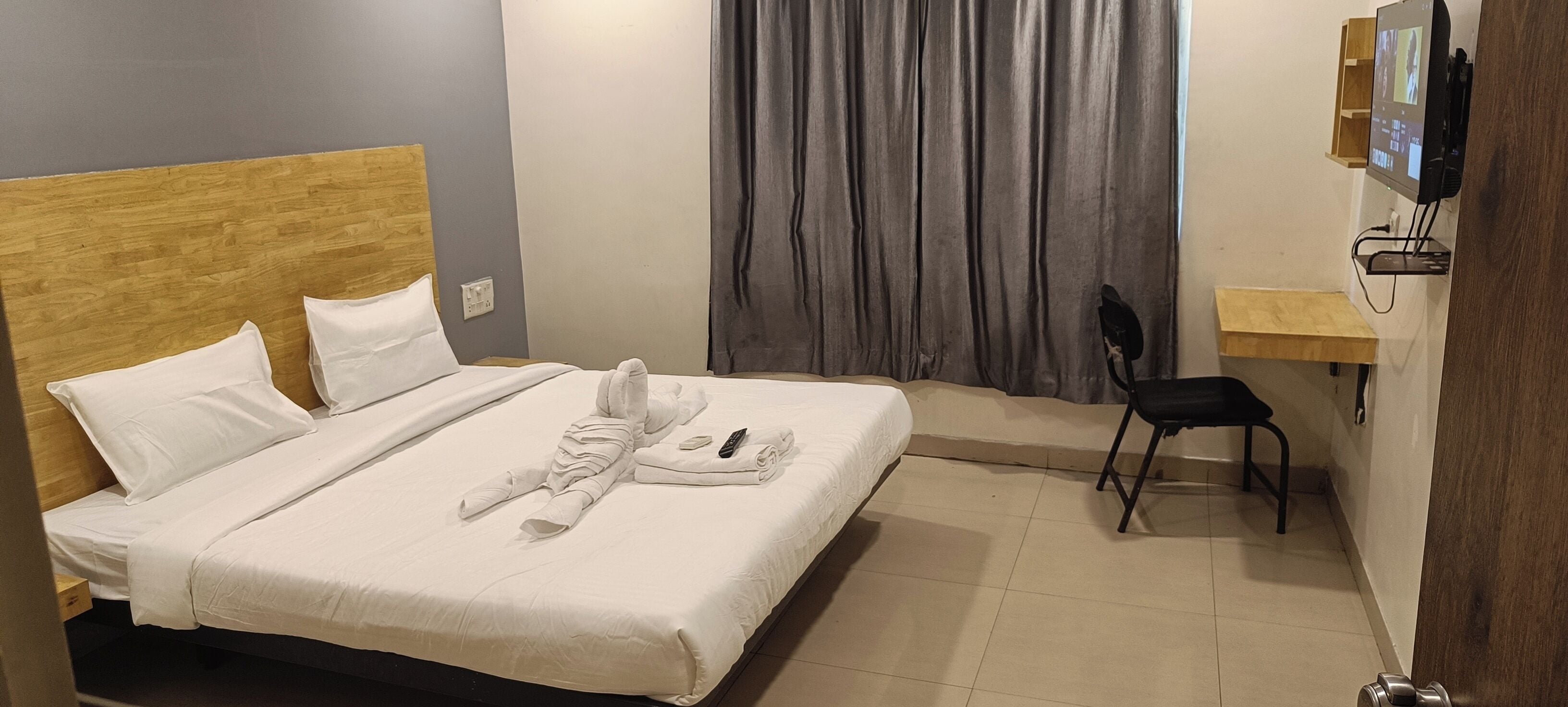 A hotel room with a bed, a desk, a chair, and a television.
