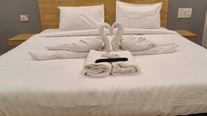 Un lit bien fait, avec des serviettes disposées en forme de cœur, un thermomètre numérique et un objet noir posé sur le lit.
