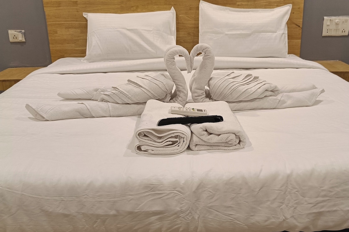 Een opgemaakt bed met handdoeken gerangschikt in de vorm van een hart, een digitaal thermometer en een zwart object op het bed.