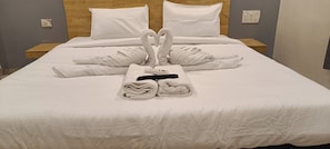 Een opgemaakt bed met handdoeken gerangschikt in de vorm van een hart, een digitaal thermometer en een zwart object op het bed.