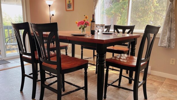 Uma sala de jantar com uma mesa e cadeiras de madeira, um vaso com flores e um quadro na parede.