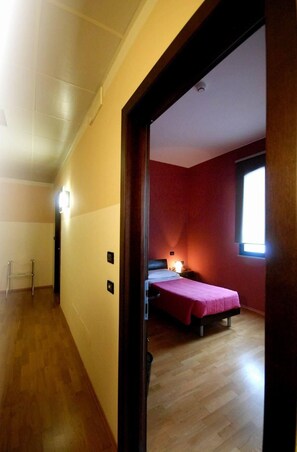 A hotel room with a wooden floor, a bed with a red bedspread, a nightstand with a lamp, and a window with natural light. - Albergo Delle Industrie (Casalmaggiore)